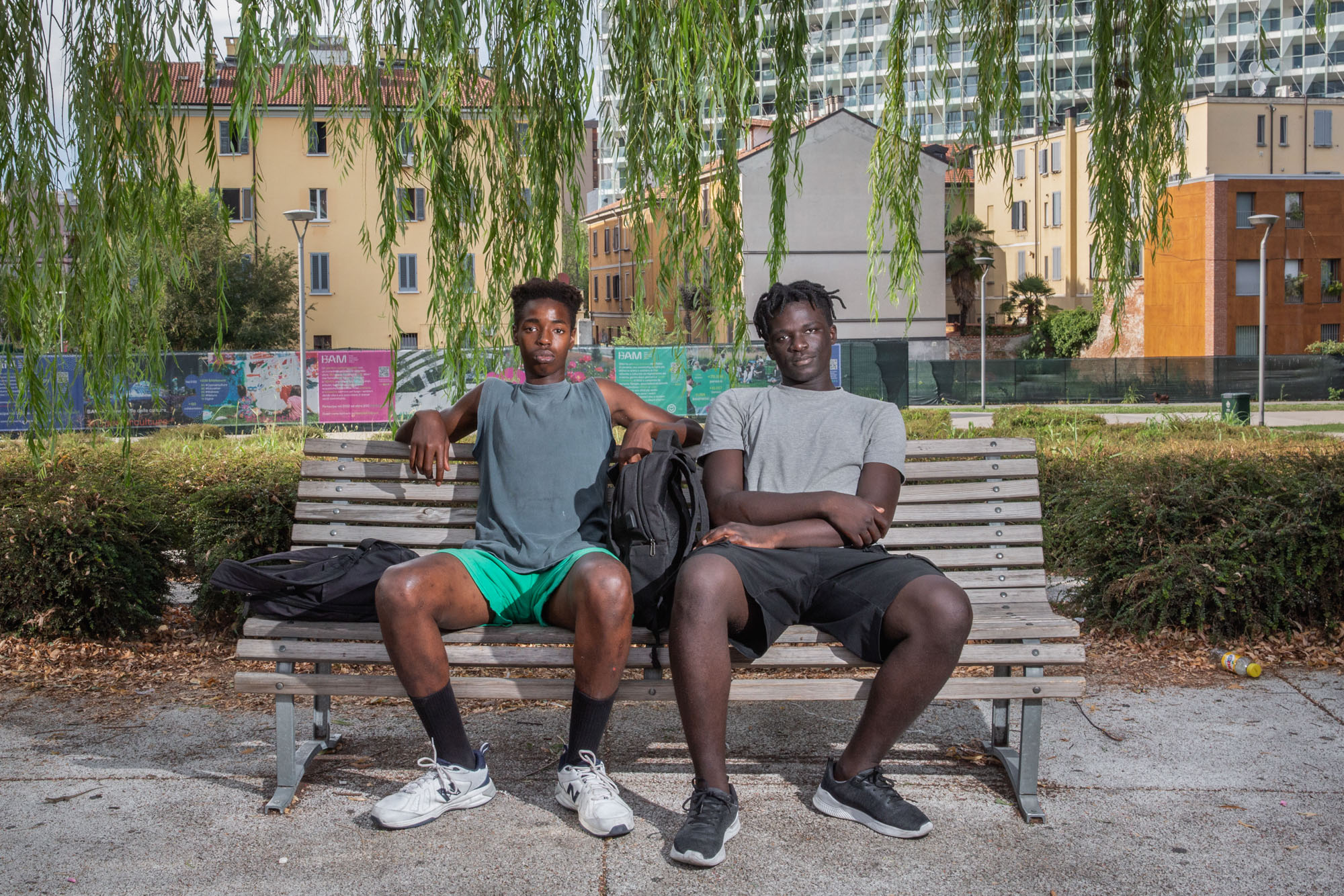 Ndongo Gueye, 18 anni, e Cheikh Badar Gueye, 19 anni, nati in Senegal e cresciuti nel nord Italia, siedono all'ombra della BAM Tree Library, un parco nel distretto finanziario di Milano. Italia, 2022 - Umidità 38%, Temperatura 35°C